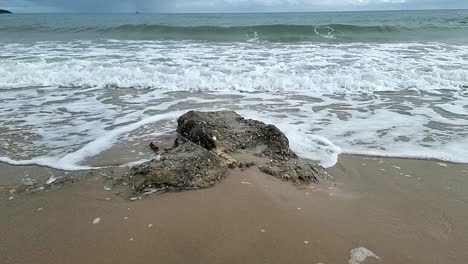 Slow-motion-foaming-sea-waves-washing-around-rugged-weathered-rock-on-Anglesey-beach-coastline
