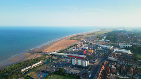 Witness-the-allure-of-Skegness,-a-coastal-gem-in-Lincolnshire,-through-aerial-footage,-featuring-its-vast-beach,-lively-tourist-area,-funfair-rides,-and-iconic-pier-on-a-summer-evening