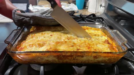 Knife-Being-Used-To-Cut-Along-Freshly-Baked-Lasagna-In-Baking-Tray-On-Cooker-Top,-static-shot