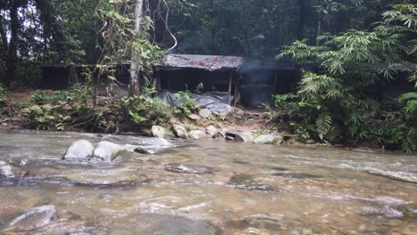 Toma-Inclinada-De-Un-Campamento-En-Una-Selva-Tropical-Con-Un-Pequeño-Río-En-Frente