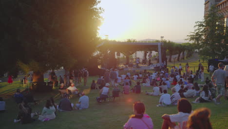 Sunset-Golden-Hour-View-of-a-Crowd-Sitting-On-Public-Park's-Grass-Lawn,-Waiting-for-a-Show-to-Begin