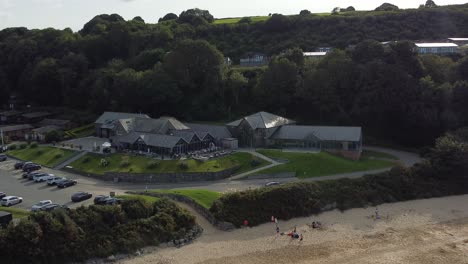 Aerial-view-zoom-in-towards-old-fashioned-tavern-style-beachfront-exclusive-restaurant-shaded-by-Welsh-mountainside-on-secluded-beach