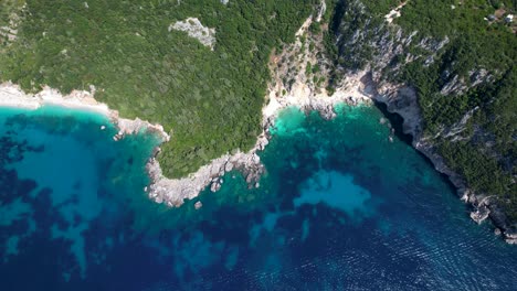 Rocky-coastline-cliff-in-Albania-surrounded-by-amazing-blue-turquoise-Ionian-sea,-colorful-sea-scene-from-above-on-beautiful-riviera
