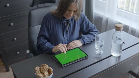 Cheerful-Blonde-Woman-Engaging-with-Tablet-Displaying-Green-Screen