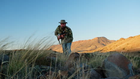Hunter-with-hunting-rifle-in-hands-stalks-prey-over-rocky-Karoo-landscape