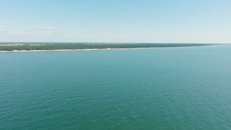 Aerial-establishing-view-of-Baltic-sea-coast-on-a-sunny-day,-distant-white-sand-seashore-and-pine-tree-forest,-wide-angle-drone-shot-moving-forward