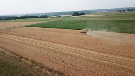 A-cinematic-4K-drone-shot-of-a-combine-harvester-harvesting-a-field-in-France,-showcasing-agriculture-with-an-epic-view-and-dramatic-dust