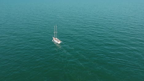 Aerial-establishing-view-of-a-white-sailboat-in-the-calm-Batltic-sea,-white-sailing-yacht-in-the-middle-of-the-boundless-sea,-sunny-summer-day,-wide-done-shot-moving-forward,-tilt-down