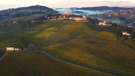 Aerial-panoramic-landscape-view-of-an-italian-medieval-castle,-surrounded-by-vineyards,-on-a-misty-morning