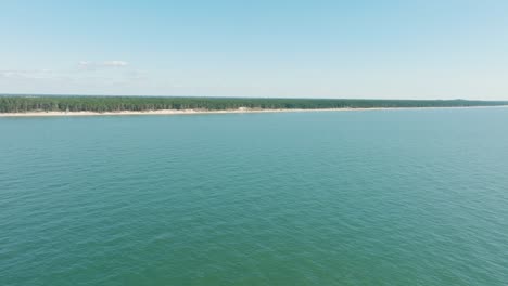 Aerial-establishing-view-of-Baltic-sea-coast-on-a-sunny-day,-distant-white-sand-seashore-and-pine-tree-forest,-wide-ascending-drone-shot-moving-forward