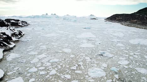 Breaking-ice-near-rocky-coastline-in-Greenland,-aerial-drone-view