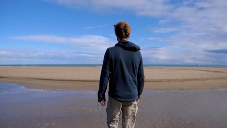 slow-motion-shot-of-a-man-walking-across-a-beach-at-low-tide-near-the-Sete-salt-flats