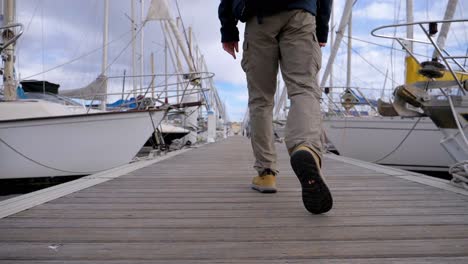 Slow-motion-low-angle-shot-of-a-man-walking-along-a-marina-dock-toward-a-yacht