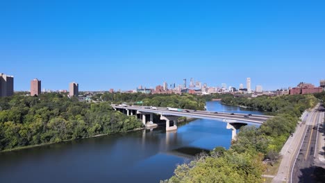 Reveal-through-the-green-trees-the-Minneapolis-skyline-in-the-summer-just-over-the-river-and-the-hiawatha-highway-and-bridges