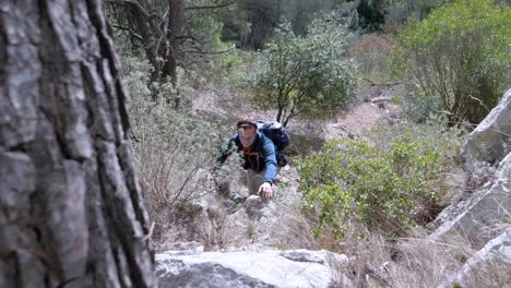 Slow-motion-shot-of-a-man-climbing-and-using-his-hands-to-get-up-the-hillside