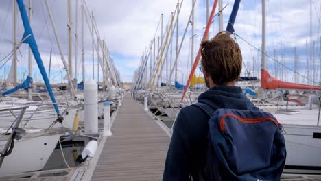 Slow-motion-shot-of-a-man-walking-along-a-marina-dock-towards-his-yacht
