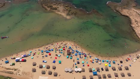 Sommertag-Am-Strand-Mit-Menschen-Im-Wasser-Und-Unter-Bunten-Sonnenschirmen,-Drohnenaufnahmen-Von-Oben-Nach-Unten