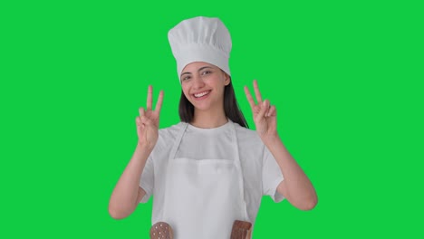 Happy-Indian-female-professional-chef-showing-victory-sign-Green-screen