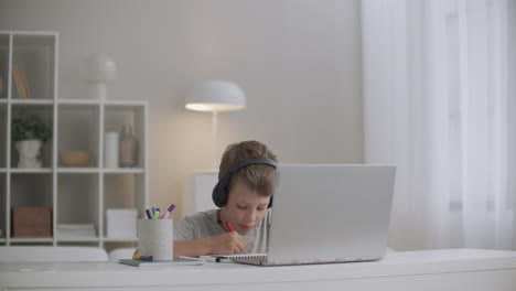 Un-Niño-Pequeño-Está-Viendo-Videos-Educativos-Para-Niños-En-Una-Computadora-Portátil-Y-Escuchando-Con-Auriculares-Dibujando-En-Papel