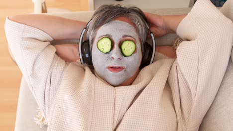 Woman-with-facial-mask-and-cucumbers-on-face-listening-to-music