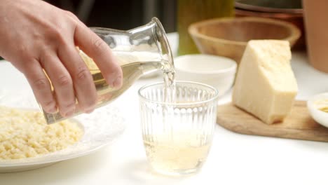Crop-chef-pouring-white-wine-for-risotto-in-glass