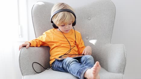 Barefoot-boy-in-headphones-watching-cartoons-on-tablet