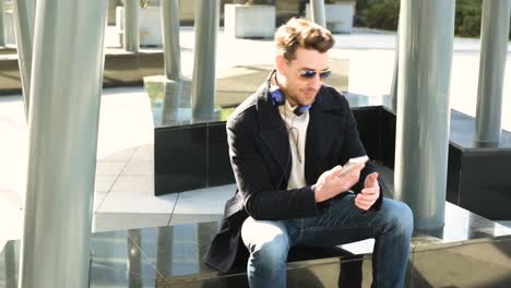 Cheerful-man-in-modern-sunglasses-with-smartphone-resting-in-town