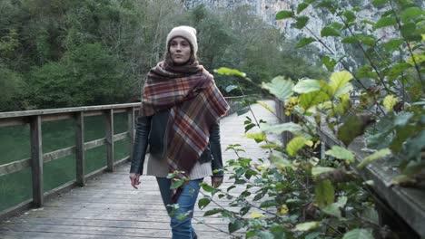 Serene-woman-in-outerwear-walking-on-footbridge-over-tranquil-lake