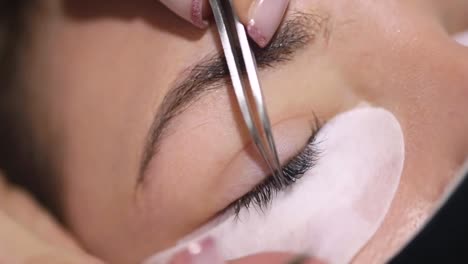 Crop-beautician-with-tweezers-applying-artificial-lash-on-client