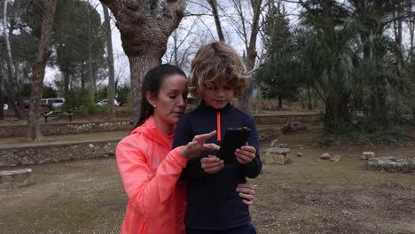 Smiling-sportswoman-with-son-on-smartphone-outdoors