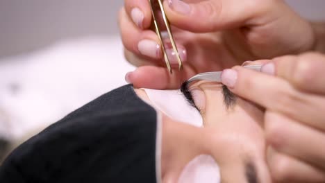 Crop-beautician-with-tweezers-applying-artificial-lash-on-client