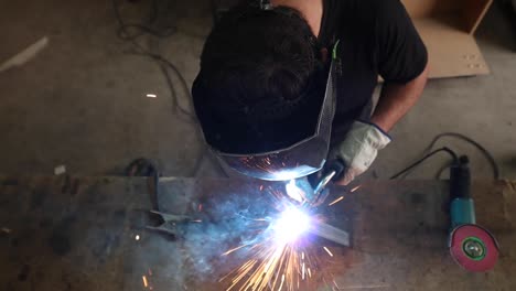 Welder-in-protective-helmet-welding-metal-detail-in-workshop