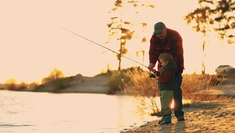 Alter-Fischer-Und-Kleiner-Junge-Angeln-Am-Ufer-Eines-Flusses-Oder-Sees-An-Einem-Sonnigen-Abend-Und-Einem-Glücklichen-Familienwochenende