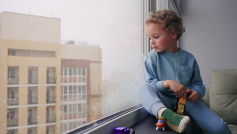 happy-four-years-toddler-is-sitting-calmly-on-windowsill-and-looking-on-street-in-winter-day-carefree-childhood