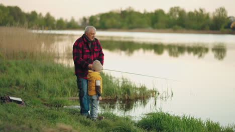 grandfather-and-little-boy-are-fishing-together-in-forest-lake-in-calm-summer-morning-happy-weekend-in-nature