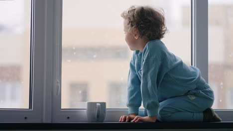 happy-and-carefree-childhood-little-boy-in-blue-pajamas-is-sitting-on-windowsill-in-apartment-in-winter-day
