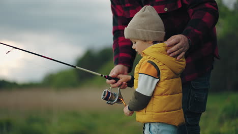 curious-little-boy-is-learning-to-catch-fish-by-rod-in-lake-grandfather-is-teaching-grandson