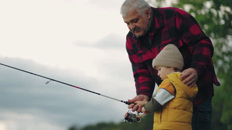 careful-grandfather-is-teaching-his-grandson-to-fishing-in-lake-family-is-resting-in-nature