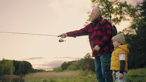 grandpa-is-teaching-his-grandson-to-fish-on-shore-of-lake-old-man-is-throwing-fishing-rod