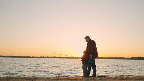 Feliz-Fin-De-Semana-Familiar-En-La-Naturaleza,-Abuelo-Y-Nieto-Están-Pescando-En-La-Orilla-Del-Río