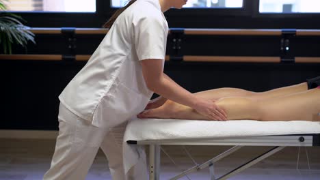 Anonymous-female-physiotherapist-massaging-leg-of-crop-woman