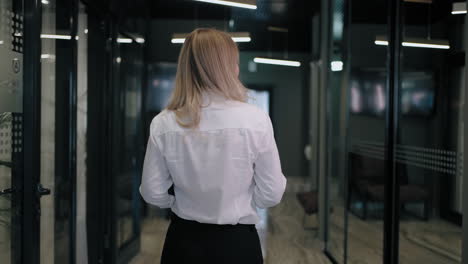 The-camera-follows-the-back-of-a-blonde-business-woman-in-a-shirt-down-the-corridor