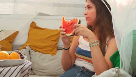 Young-woman-eating-fresh-watermelon-in-backyard-tent