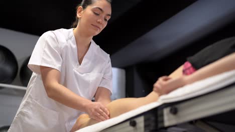Smiling-female-physiotherapist-massaging-leg-of-crop-woman