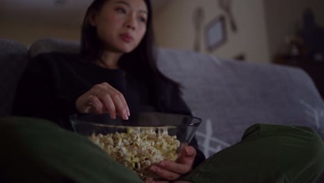 Young-Asian-woman-sitting-on-sofa-and-eating-popcorn