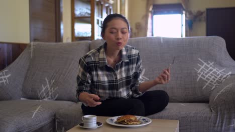 Ethnic-woman-eating-tasty-pancakes-in-living-room