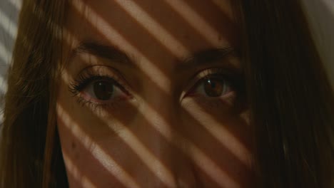 Woman-blinking-and-smiling-in-shadows-of-blinds