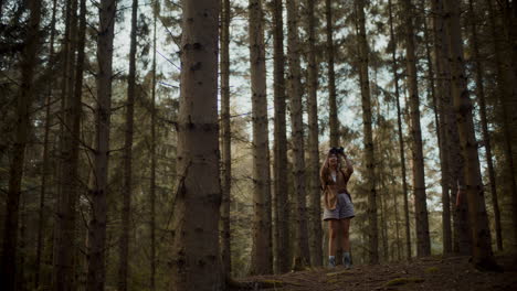 Female-explorer-searching-through-binoculars-amidst-trees