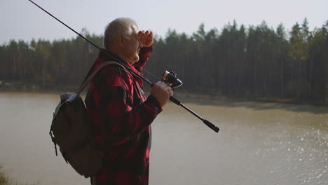 tourist-man-is-viewing-river-or-lake-in-forest-at-sunny-autumn-day-covering-face-from-sun-by-palm-fisherman-on-shore-of-reservoir