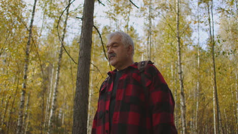 grey-haired-man-with-moustache-is-strolling-in-forest-at-autumn-day-enjoying-nature-and-landscape-exploring-nature-reserve